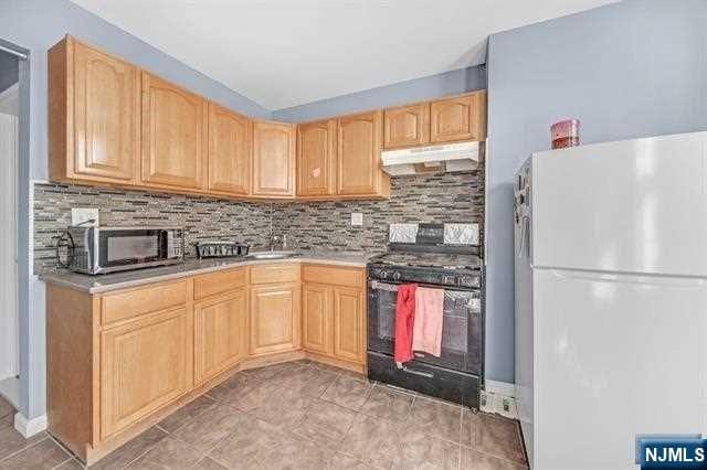 kitchen with white refrigerator, sink, black electric range, decorative backsplash, and light brown cabinetry