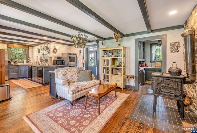 living room featuring beamed ceiling, a healthy amount of sunlight, brick wall, and hardwood / wood-style flooring