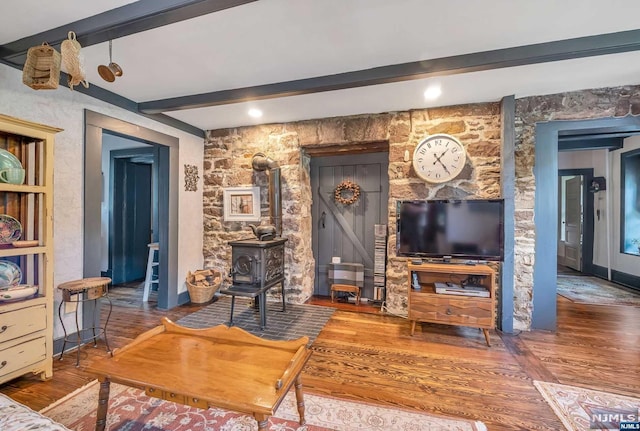 living room featuring beamed ceiling, wood-type flooring, and a wood stove