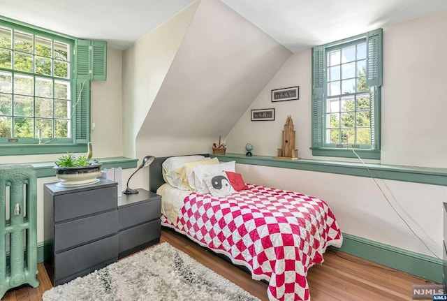 bedroom featuring multiple windows, hardwood / wood-style floors, lofted ceiling, and radiator