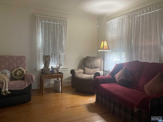 living area with a healthy amount of sunlight, wood-type flooring, and ornamental molding