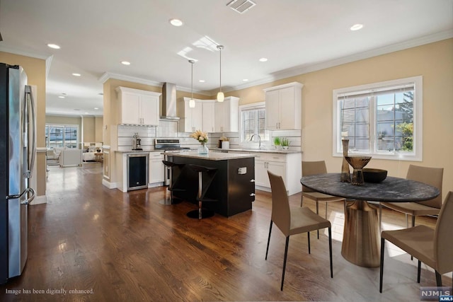 kitchen with white cabinets, wall chimney exhaust hood, hanging light fixtures, and a kitchen island