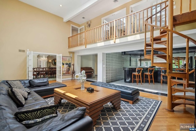 living room with beam ceiling, a chandelier, a high ceiling, and hardwood / wood-style flooring