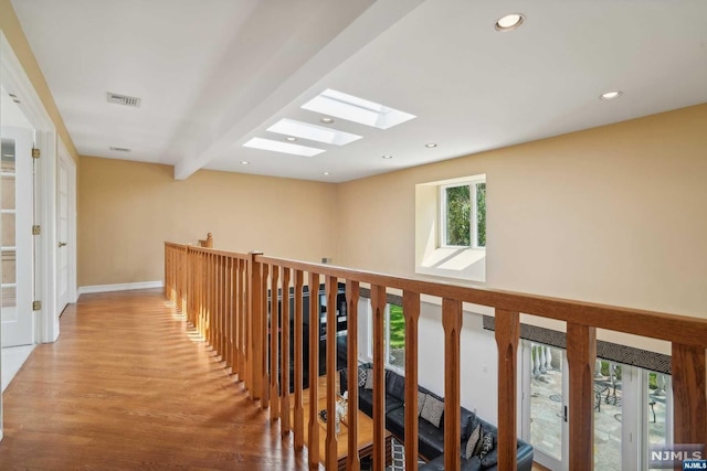 corridor with hardwood / wood-style floors, beamed ceiling, and a skylight