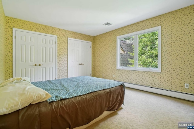 bedroom with carpet flooring, two closets, and a baseboard heating unit