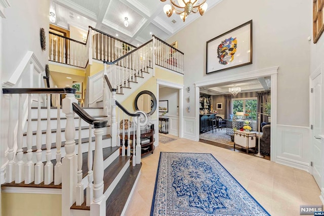 foyer entrance with ornamental molding, a high ceiling, a notable chandelier, and coffered ceiling