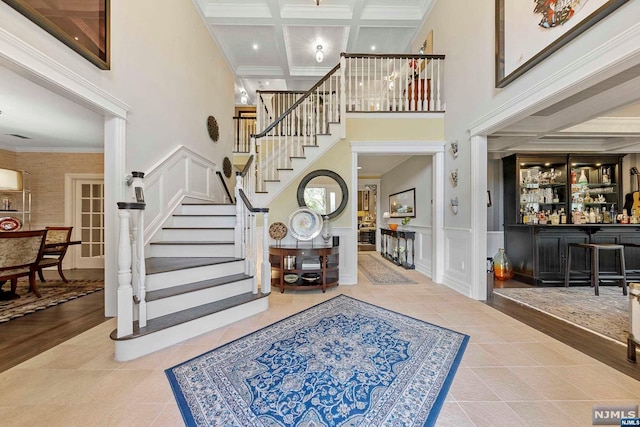 foyer entrance featuring ornamental molding, coffered ceiling, hardwood / wood-style flooring, a high ceiling, and bar