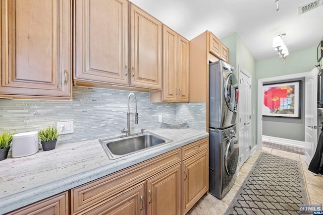 kitchen featuring sink, stacked washer and dryer, decorative backsplash, light tile patterned flooring, and light stone counters