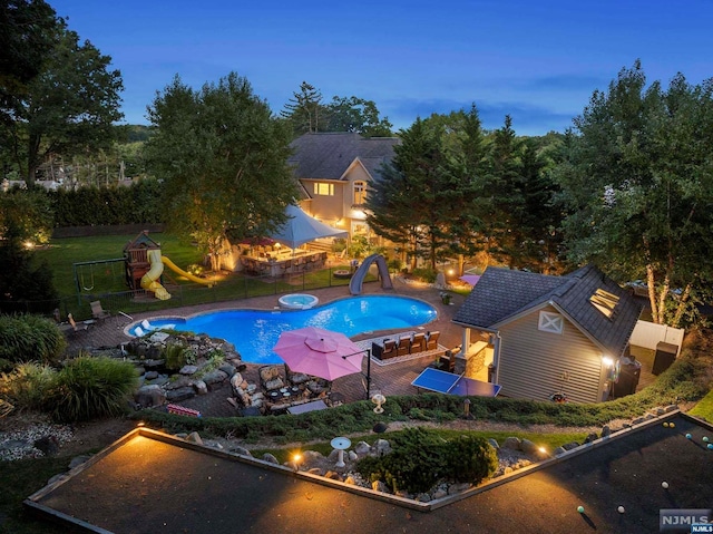 pool at dusk featuring a yard, an outdoor structure, and a water slide