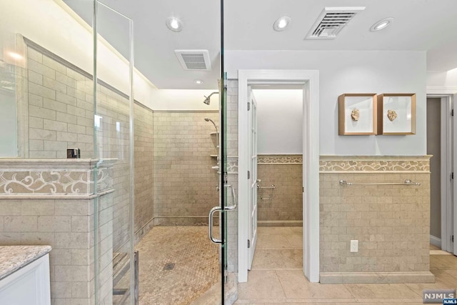 bathroom featuring tile patterned flooring, vanity, an enclosed shower, and tile walls