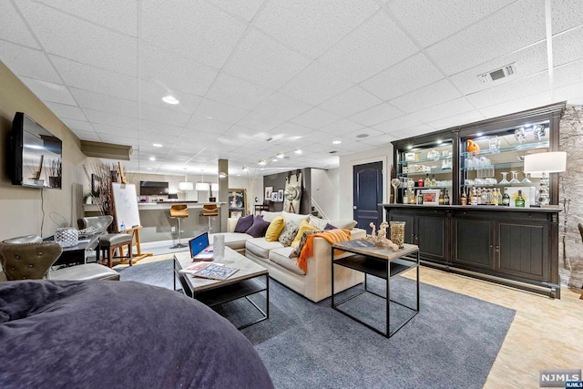 living room with a drop ceiling, indoor bar, and hardwood / wood-style flooring