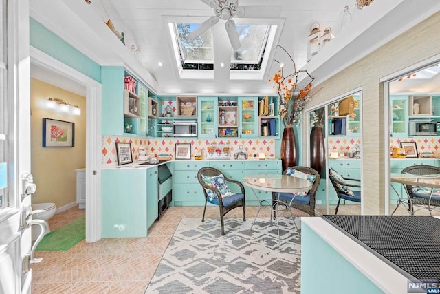 kitchen with ceiling fan, decorative backsplash, ornamental molding, and a skylight