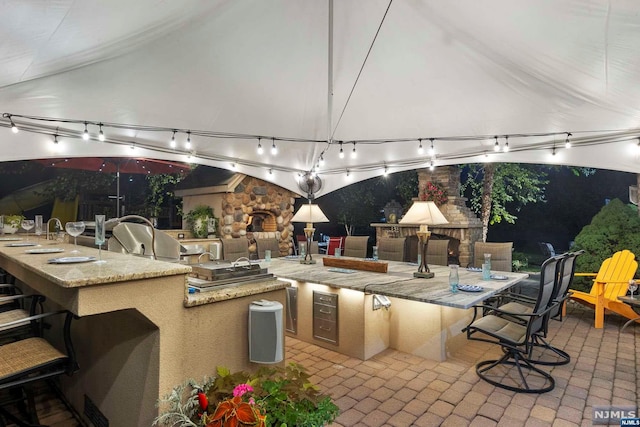 view of patio / terrace featuring an outdoor stone fireplace, a bar, and an outdoor kitchen