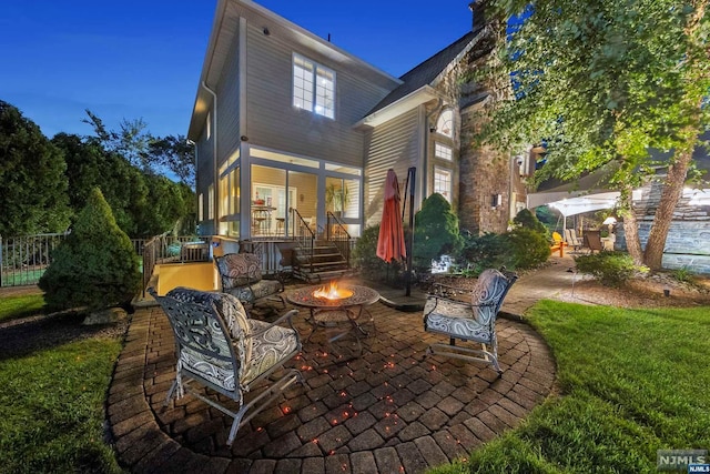 back house at dusk featuring a fire pit, a porch, a yard, and a patio