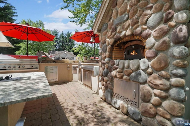 view of patio with an outdoor stone fireplace, an outdoor kitchen, and a grill