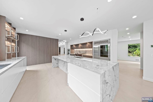 kitchen with built in fridge, sink, decorative light fixtures, a large island, and light stone counters