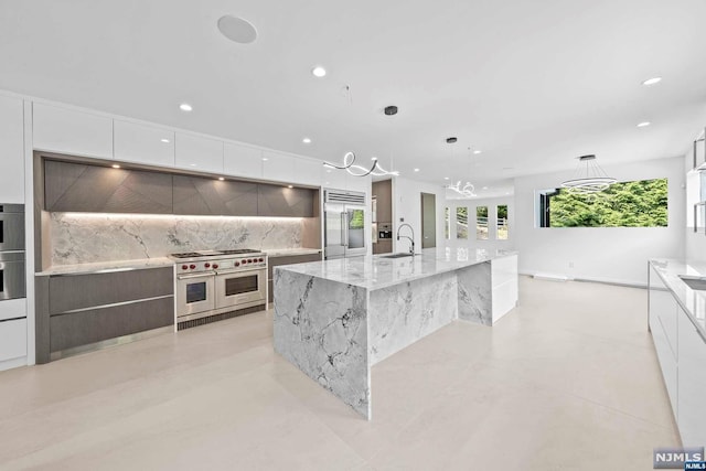 kitchen featuring pendant lighting, high end appliances, a large island with sink, sink, and white cabinetry