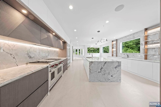 kitchen featuring double oven range, white cabinets, sink, light stone countertops, and decorative light fixtures