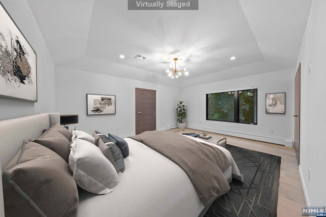 bedroom featuring a raised ceiling, light hardwood / wood-style flooring, and an inviting chandelier