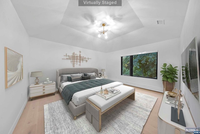 bedroom featuring a raised ceiling, a chandelier, light hardwood / wood-style floors, and lofted ceiling