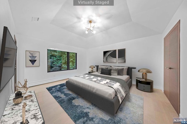 bedroom featuring hardwood / wood-style floors, an inviting chandelier, a raised ceiling, vaulted ceiling, and a baseboard radiator