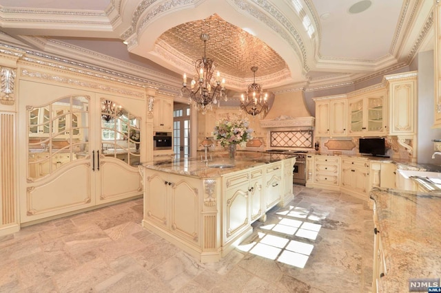 kitchen with french doors, crown molding, decorative light fixtures, cream cabinetry, and a kitchen island with sink