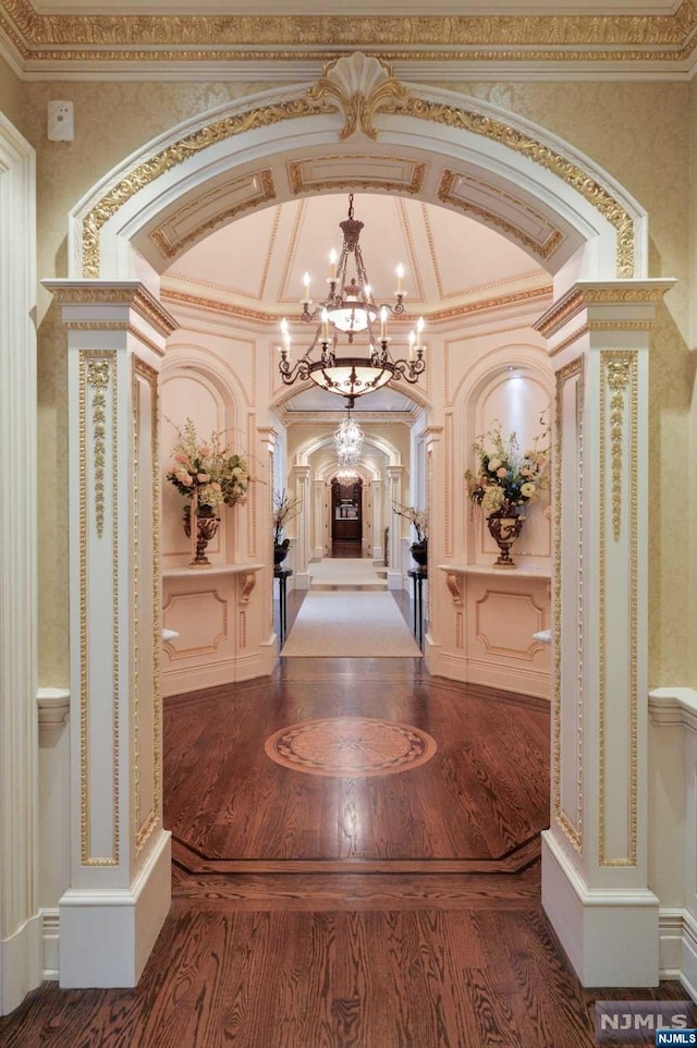 hall featuring decorative columns, hardwood / wood-style floors, an inviting chandelier, and ornamental molding