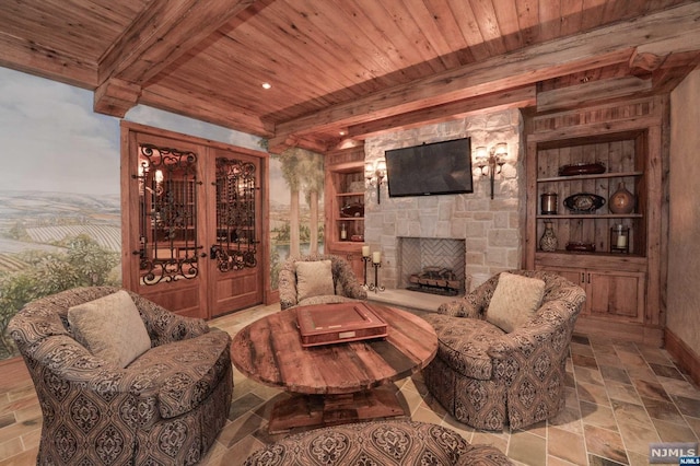 living area with built in shelves, a stone fireplace, wooden ceiling, and beam ceiling