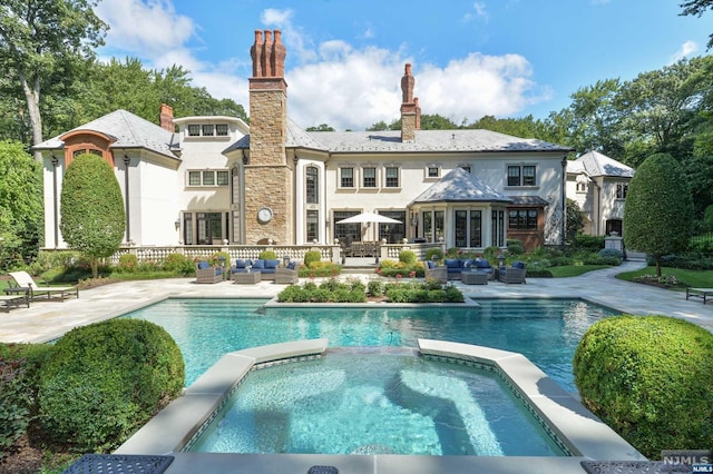 rear view of house featuring a swimming pool with hot tub, an outdoor living space, and a patio