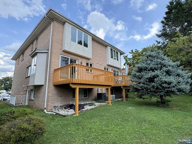 rear view of property featuring central air condition unit, a wooden deck, and a lawn