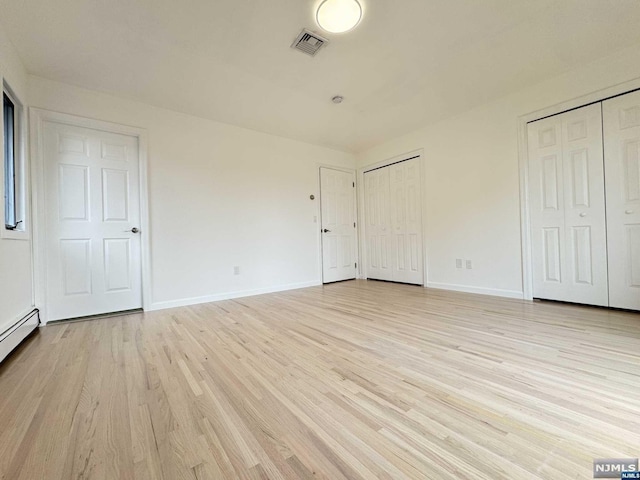 unfurnished bedroom with a baseboard radiator, light hardwood / wood-style flooring, and multiple closets