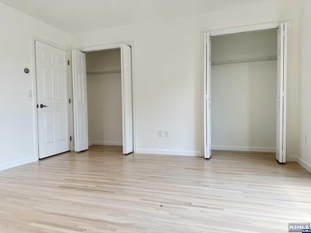 unfurnished bedroom with light wood-type flooring and multiple closets