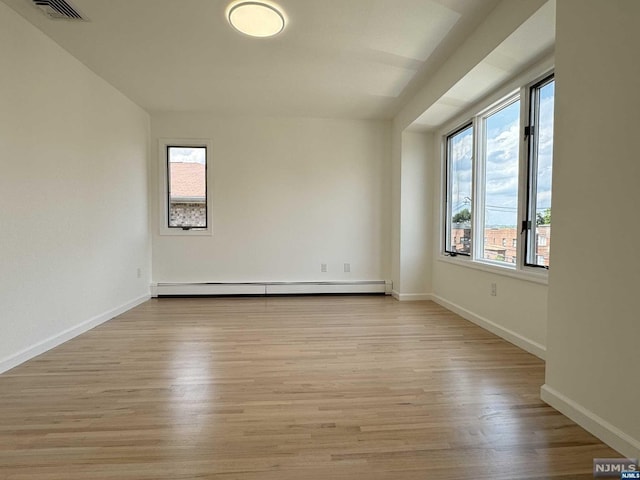 empty room with a healthy amount of sunlight, a baseboard radiator, and light hardwood / wood-style floors