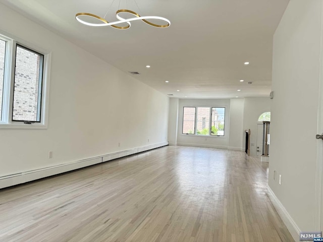 unfurnished room with light hardwood / wood-style floors, an inviting chandelier, and a baseboard heating unit