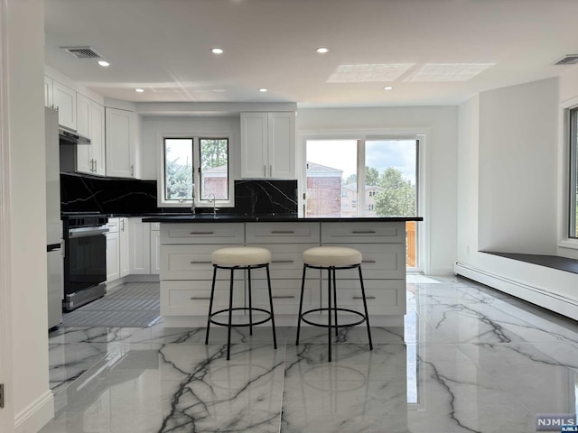 kitchen with decorative backsplash, stainless steel stove, white cabinetry, and a wealth of natural light