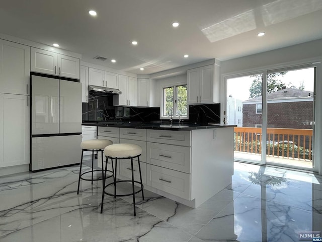 kitchen featuring white fridge, white cabinetry, tasteful backsplash, and a breakfast bar area