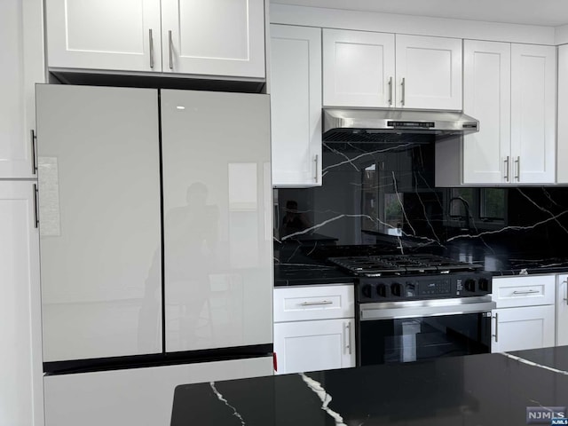 kitchen with dark stone counters, white cabinets, stainless steel gas stove, decorative backsplash, and white fridge