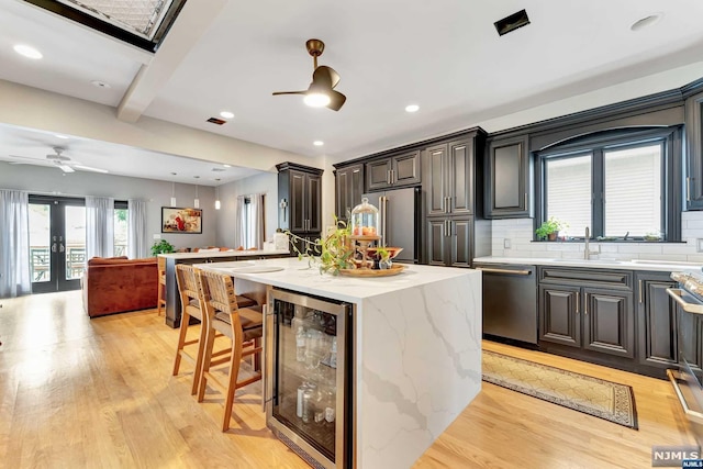 kitchen with decorative backsplash, stainless steel appliances, beverage cooler, light hardwood / wood-style flooring, and a center island