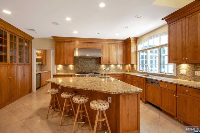 kitchen featuring decorative backsplash, appliances with stainless steel finishes, light stone counters, sink, and a center island with sink