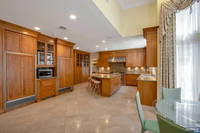 kitchen with light stone countertops, tasteful backsplash, an island with sink, a kitchen bar, and high end stainless steel range