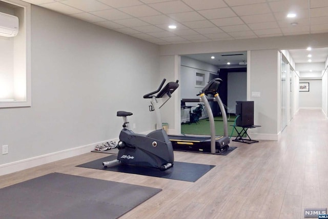 exercise room with a paneled ceiling, light hardwood / wood-style floors, and a wall unit AC