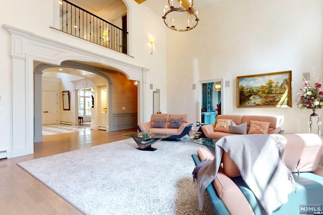 living room with baseboard heating, light hardwood / wood-style flooring, a high ceiling, and a notable chandelier