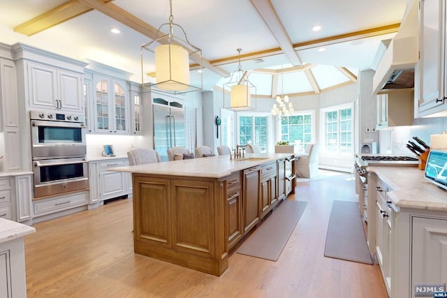 kitchen with white cabinets, light wood-type flooring, an island with sink, decorative light fixtures, and premium appliances