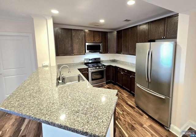 kitchen with sink, hardwood / wood-style flooring, light stone counters, kitchen peninsula, and stainless steel appliances