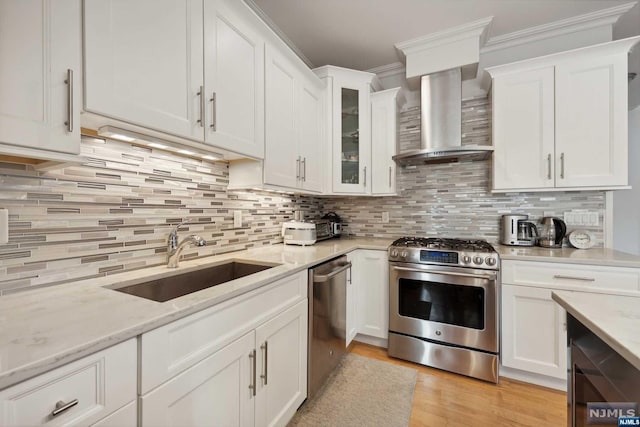 kitchen with sink, stainless steel appliances, wall chimney range hood, light stone counters, and white cabinets