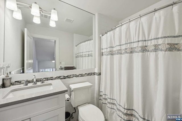 bathroom featuring vanity, toilet, and tile walls