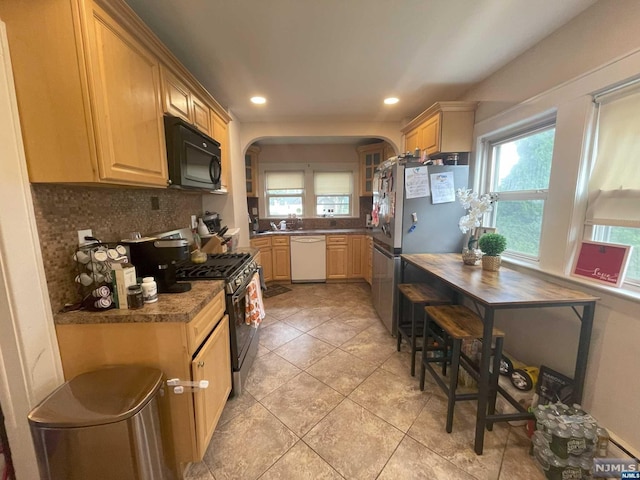 kitchen featuring backsplash, light brown cabinetry, light tile patterned floors, and appliances with stainless steel finishes