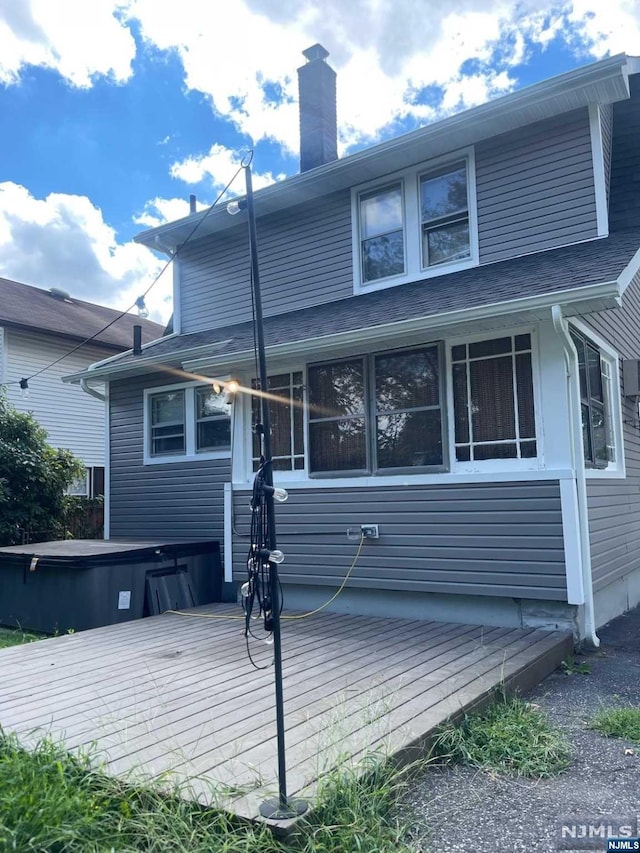 rear view of house featuring a hot tub and a deck