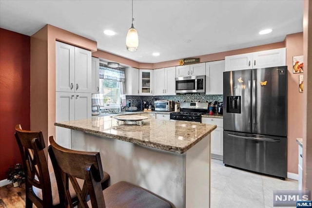 kitchen featuring a kitchen breakfast bar, white cabinetry, stainless steel appliances, and hanging light fixtures