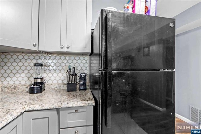 kitchen featuring white cabinetry, backsplash, black fridge, and hardwood / wood-style flooring